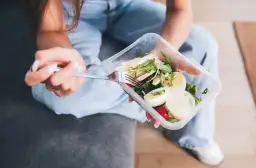 Kobieta je sałatkę z kurczakiem i jajkiem z pojemnika. To przykład self catering – samodzielnego przygotowania posiłków.