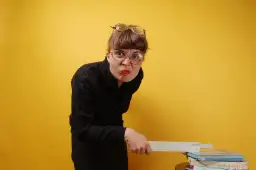 Kobieta w okularach i czarnej bluzce trzyma linijkę nad stosem książek.