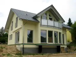 Nowy dom z żółtą elewacją i dachem w kształcie litery L. Duże okna i balkon dodają mu nowoczesnego charakteru.