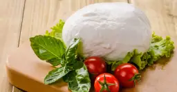 Kulista mozzarella, pomidorki i bazylia na desce. Czy mozzarella ma dużo białka? Tak, to świetne źródło białka!