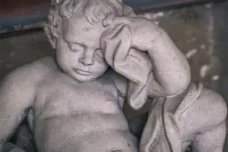 Kamienna rzeźba dziecka z zasłoniętymi oczami, jakby śniło o śmierci rodziców.
