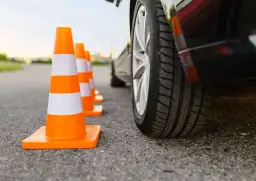 Pomarańczowe pachołki drogowe ustawione w rzędzie obok samochodu na placu manewrowym.