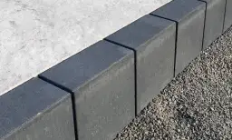 Szare obrzeża na podjazd, wykonane z kostki, oddzielają beton od żwiru.