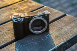 Czarny aparat Sony ZV-E10 II bez obiektywu leży na drewnianym stole, oświetlony ciepłym, zachodzącym słońcem.