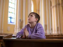 Chłopiec w fioletowej bluzie modli się w kościele, patrząc w górę.