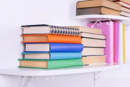 Stos kolorowych książek na półce. Czytanie między wierszami odmowy, jak objawy odrzucenia maszynopisu, bywa trudne.