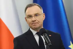 Prezydent Andrzej Duda w garniturze przed mikrofonem, w tle flagi Polski i UE.