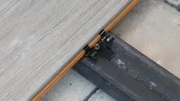 Detale montażu deski kompozytowej bez legarów. Widoczny klips mocujący deskę do czarnej belki konstrukcyjnej.