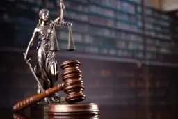 Figurka Temidy i młotek sędziowski na tle regałów z książkami prawniczymi.