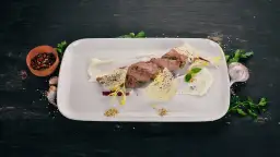 Pokrojona cielęcina z kremowym sosem, chrupiącymi dodatkami i ziołami na białym talerzu.