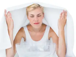 Kobieta z zamkniętymi oczami wykonuje inhalację nad miską z gorącą wodą, przykryta ręcznikiem.