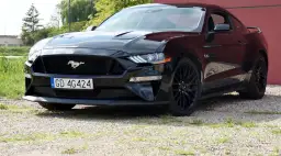 Czarny Ford Mustang z polską tablicą rejestracyjną stoi na żwirowej nawierzchni.