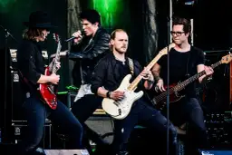 Zespół gra na scenie, wokalista śpiewa, gitarzyści i basista tworzą muzykę. Może to piosenka "Kocham Cię".