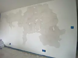 Farba odchodzi przy malowaniu wałkiem, tworząc plamy na ścianie. Widać też niebieskie osłony gniazdek i taśmę malarską.