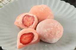 Różowe mochi z truskawkami na szarym talerzu.