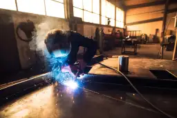Spawacz w masce ochronnej spawa metal, tworząc jasne iskry i dym w warsztacie.