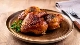 Złociste, pieczone udka z kurczaka na blasze, podane na talerzu z natką pietruszki.