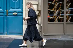 Elegancka kobieta w czarnej spódnicy plisowanej i białych mokasynach przemierza ulicę. Stylowe spódnica plisowana stylizacje.