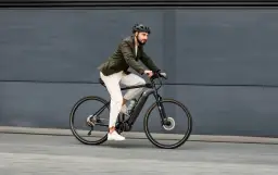 Mężczyzna w kasku i marynarce jedzie na rowerze elektrycznym po szarym tle.