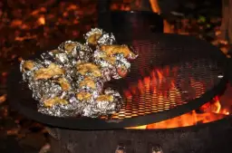 Ziemniaki zawinięte w folię aluminiową pieką się nad ogniskiem na metalowej kratce.
