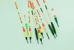 Różnokolorowe spławiki wędkarskie ułożone na jasnym tle.