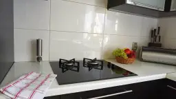 Nowoczesna kuchnia z płytkami na ścianie, płytą grzewczą, koszykiem owoców i młynkiem do pieprzu.