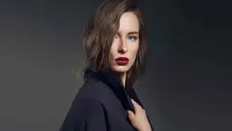 Kobieta o chłodnym typie urody zima, z niebieskimi oczami i ciemnymi ustami, w czarnym płaszczu.