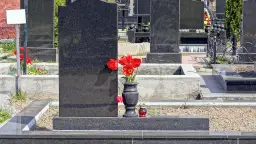Cmentarz z nagrobkami z czarnego granitu, wazon z czerwonymi tulipanami i znicz.