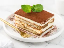 Pyszny kawałek tiramisu z mascarpone, posypany kakao i udekorowany miętą. Idealny na deser, gdy szukasz sprawdzonego przepisu.