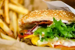Soczysty burger wołowy z serem, warzywami i frytkami w papierowym opakowaniu.