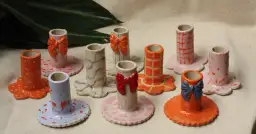 Urocze prace z gliny: świeczniki w pastelowych kolorach, ozdobione kokardkami i fantazyjnymi wzorami.