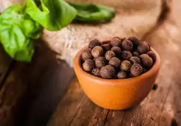 Miseczka pełna ziaren ziela angielskiego, jednego z aromatycznych spices po polsku, na drewnianym blacie.