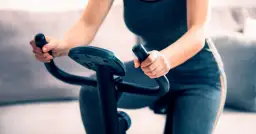 Kobieta wykonuje trening na rowerze stacjonarnym, trzymając kierownicę.