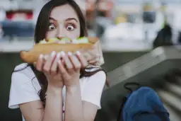 Zaskoczona dziewczyna trzyma duży kebab, zastanawiając się, ile kosztuje.