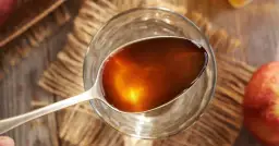 Łyżka z bursztynowym octem jabłkowym nad szklanką. Dowiedz się, jak stosować ocet jabłkowy dla zdrowia i urody.