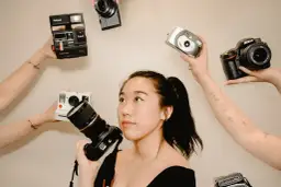 Kobieta z aparatem w ręku, otoczona przez inne aparaty: Polaroid, Nikon, cyfrówki. Idealna do wyboru, jaka lustrzanka na początek.