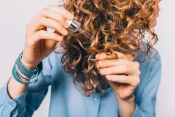 Kobieta z kręconymi włosami aplikuje serum. Czy serum do włosów się spłukuje? To pytanie nurtuje wiele osób dbających o fryzurę.