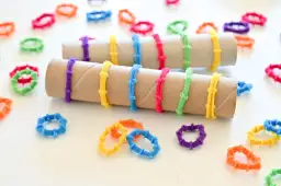 Kolorowe koralikowe pierścionki, które można zrobić z rolek po papierze toaletowym, ozdabiają rolki i leżą na białym tle.