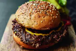 Soczysty burger wołowy z sezamową bułką i karmelizowaną cebulą na drewnianej desce.