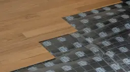 Układanie paneli podłogowych, pokazujące podkład i fragment gotowej podłogi. Dowiedz się, jak zakleić dziurę w panelu podłogowym.