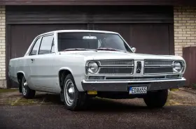En vit, klassisk Plymouth Valiant står parkerad framför ett garage.