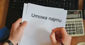 Ręka pisze długopisem na umowie najmu, obok kalkulator i laptop. Czas pomyśleć o podatku od najmu.