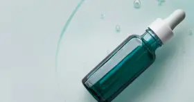 Szklana buteleczka z pipetką, wypełniona zielonym serum, na tle płynu z bąbelkami.