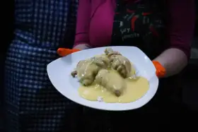 Porcja potrawki z kurczaka w kremowym sosie, podana na ryżu. Danie prezentowane na białym talerzu, trzymanym przez osobę w pomarańczowych rękawiczkach.