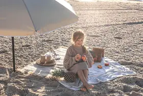 Dziewczynka na plaży pod parasolem, z owocami i ananasem. Idealne rzeczy, co zabrać na wakacje nad morze z dzieckiem.