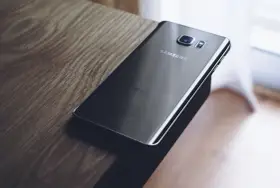 Czarny Samsung leży na drewnianym blacie. Chcesz wiedzieć, jak zresetować telefon Samsung?