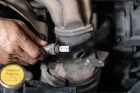 Mechanik trzyma w dłoni sondę lambda, przygotowując ją do czyszczenia.