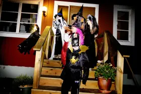 Barn utklädda till häxor och Batman förbereder sig för halloween helg. En svart katt smyger på trappan.