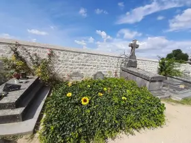 La tombe de Van Gogh, recouverte de verdure et ornée de tournesols, sous un ciel bleu.