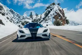 Biały Koenigsegg Agera RS z czarnym pasem na masce pędzi po ośnieżonej górskiej drodze.